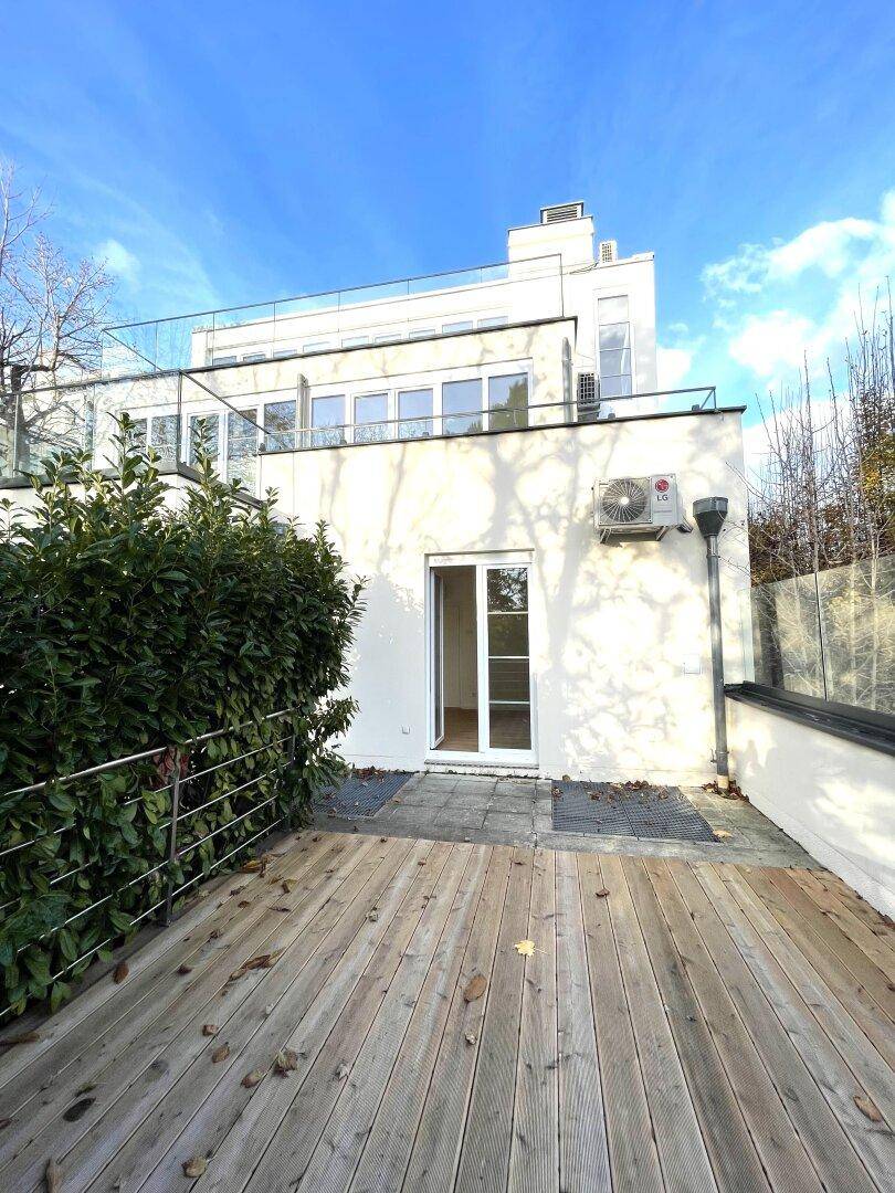 Hinterer Bereich des Hauses mit Holzterrasse, Klimaanlage und Blick auf die moderne Architektur.