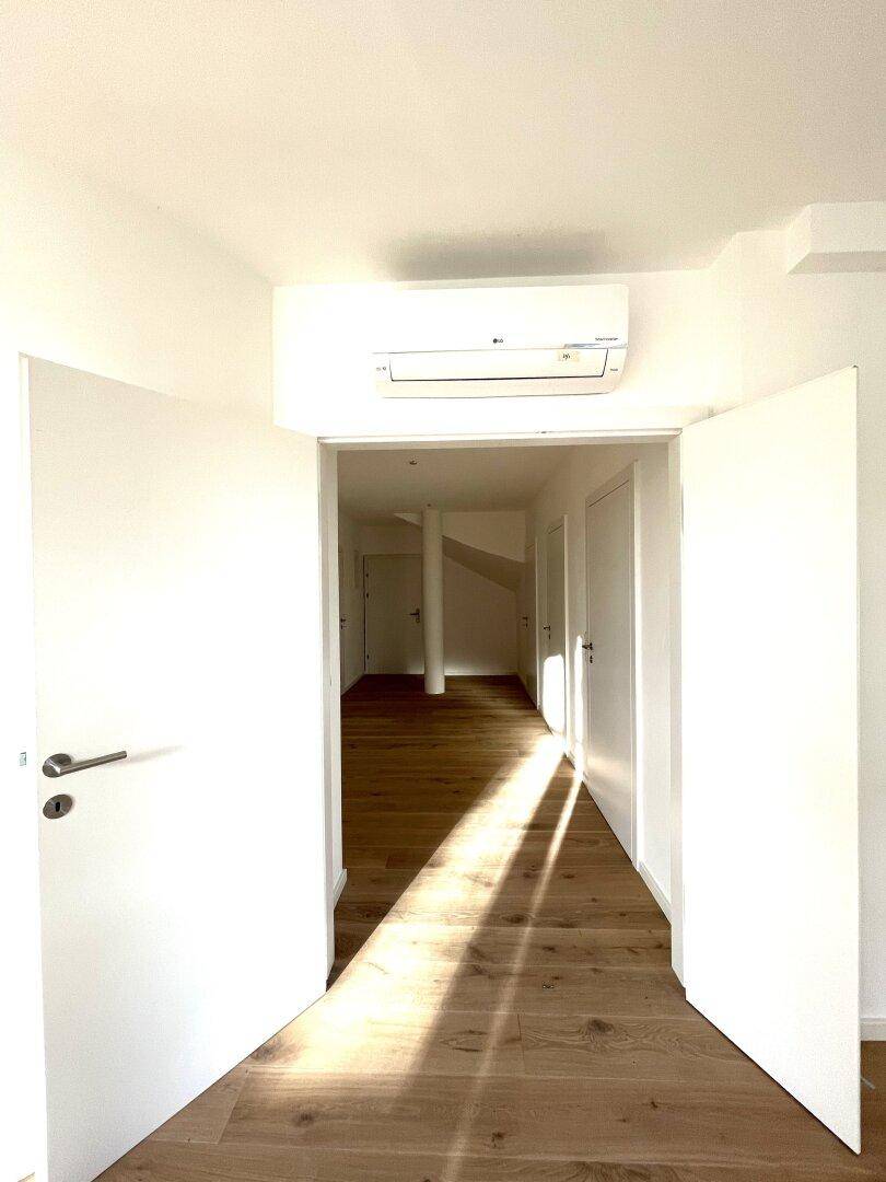 Eingangsbereich des Flurs mit Klimaanlage über der Tür und hellem Holzboden.