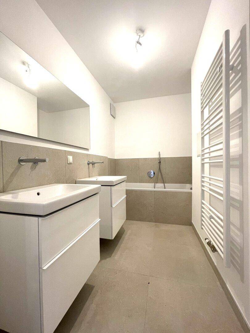 Modernes Badezimmer mit Doppelwaschbecken, Badewanne und praktischem Handtuchheizkörper.