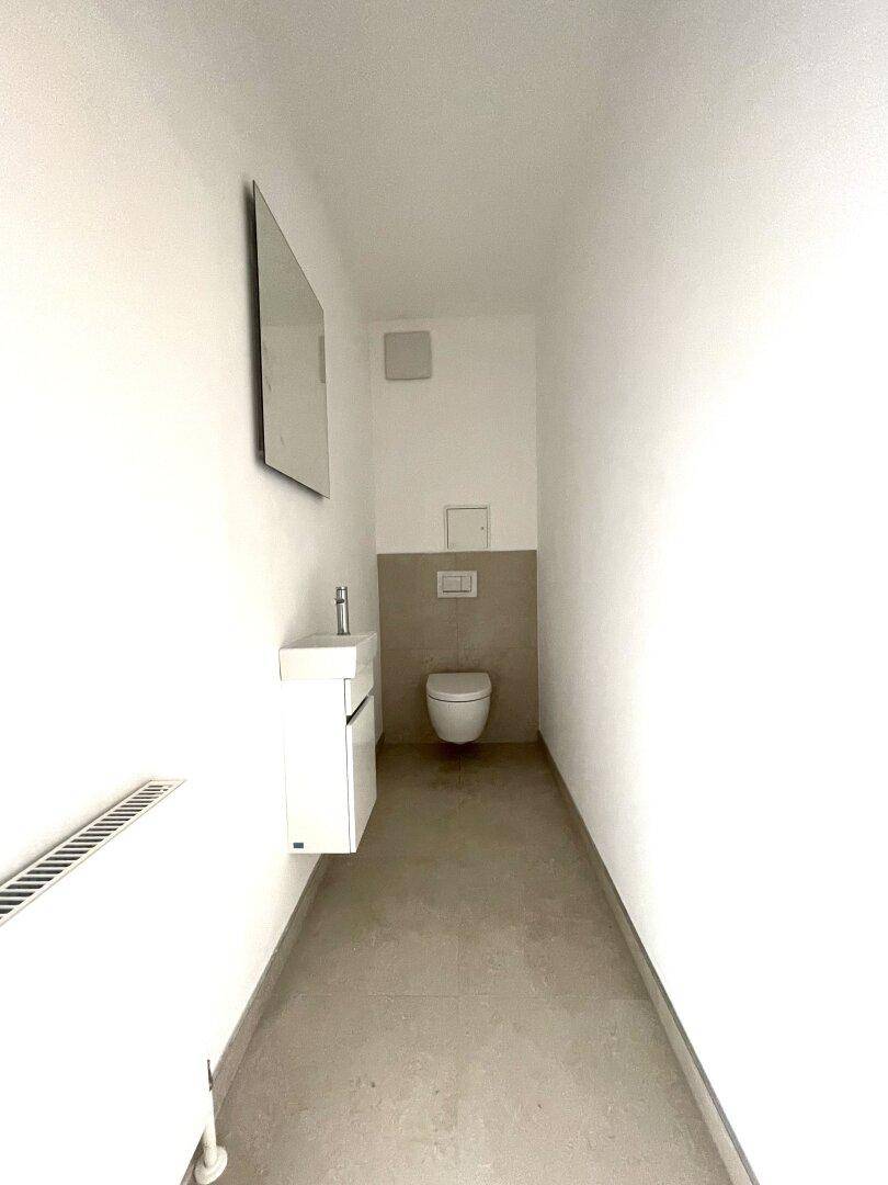 Schmale Gästetoilette mit wandhängendem WC und kleinem Waschbecken in modernem Design.