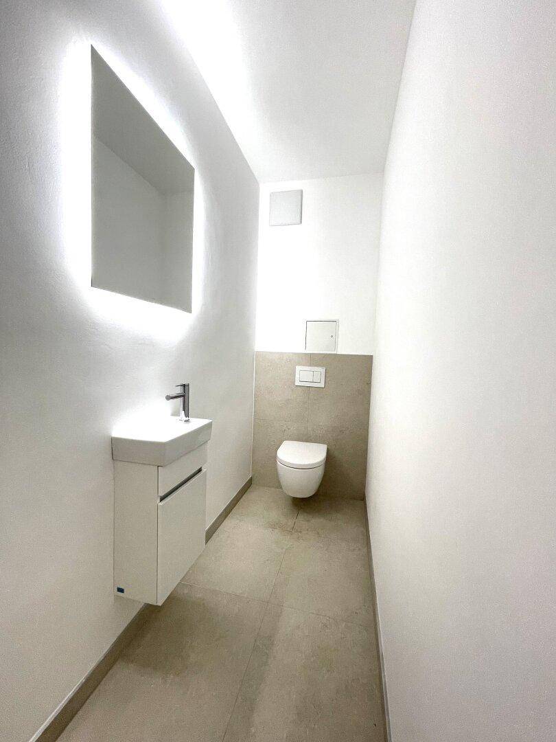 Moderne Gästetoilette mit beleuchtetem Spiegel, wandhängendem WC und eleganten Fliesen.