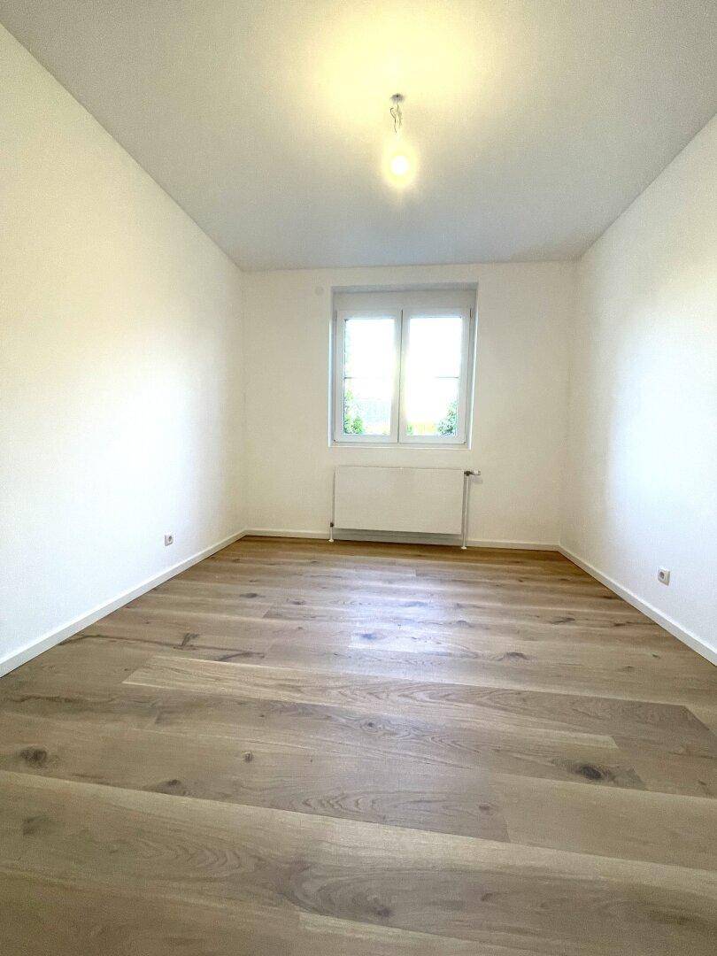 Leeres Zimmer mit hellem Holzboden und einem Fenster, ideal als Schlaf- oder Arbeitszimmer.