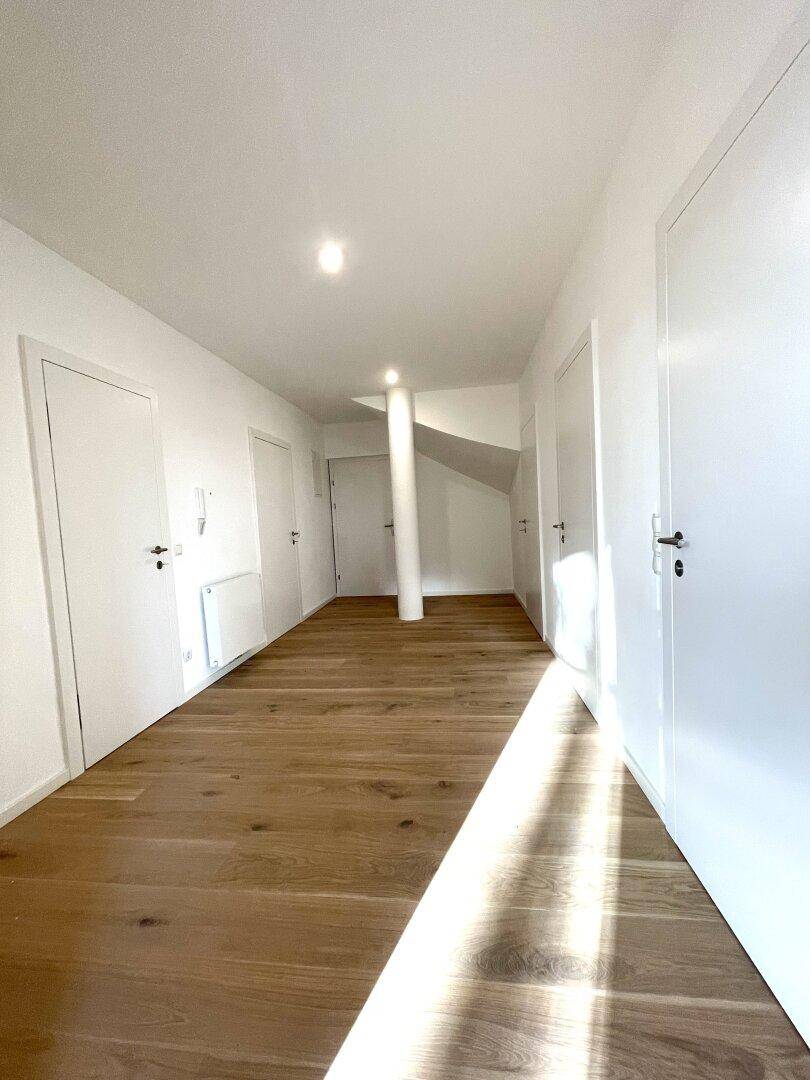 Geräumiger Flur mit Holzboden, weißen Wänden und Türen, durchflutet von Sonnenlicht.
