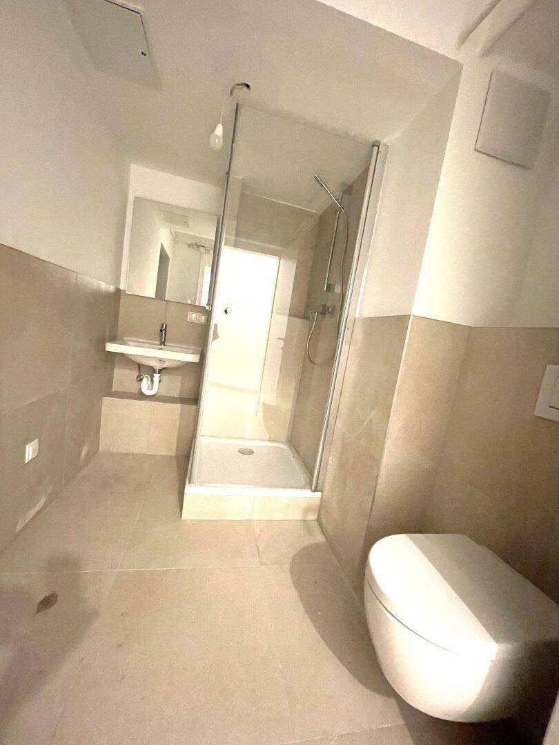 Modernes Badezimmer mit Duschkabine, wandhängendem WC und beigefarbenen Fliesen.