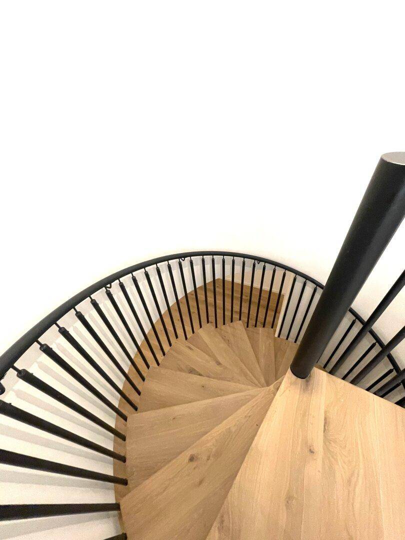 Elegante Wendeltreppe mit Holzstufen und schwarzem Metallgeländer, ein architektonisches Highlight.