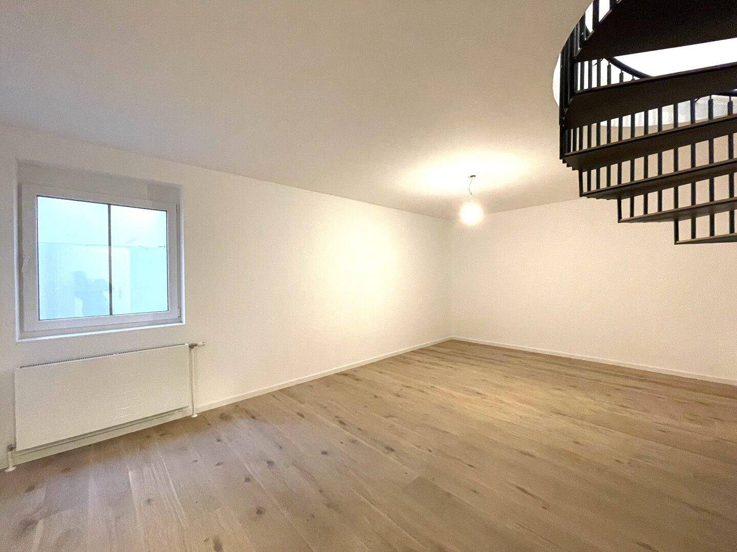 Geräumiges Zimmer mit Holzboden, Fenster und Blick auf die moderne Wendeltreppe.