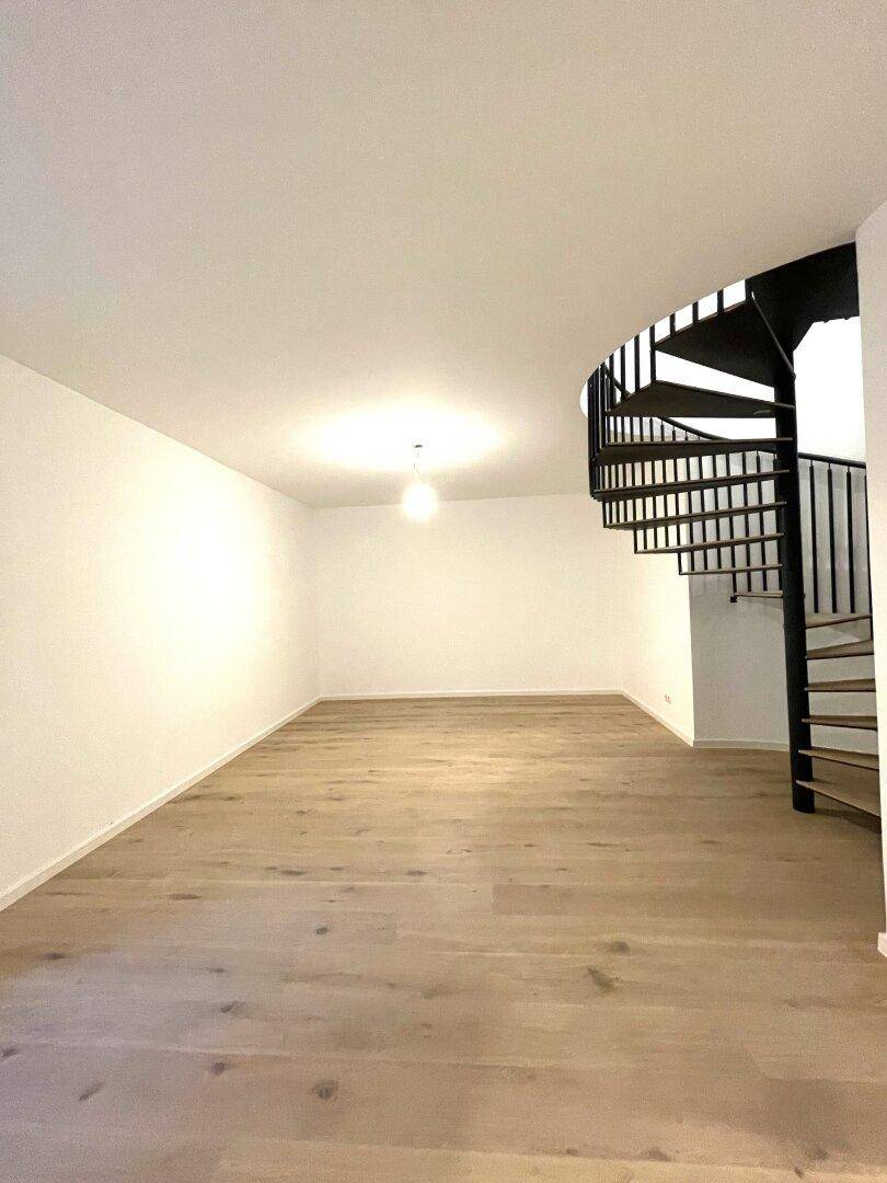 Heller Wohnraum mit Holzparkettboden und eleganter schwarzer Wendeltreppe.