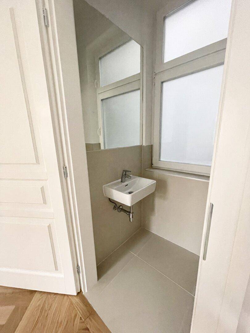 Kleines Gäste-WC mit Fenster, modernem Waschbecken und hellen Fliesen an Wänden und Boden.