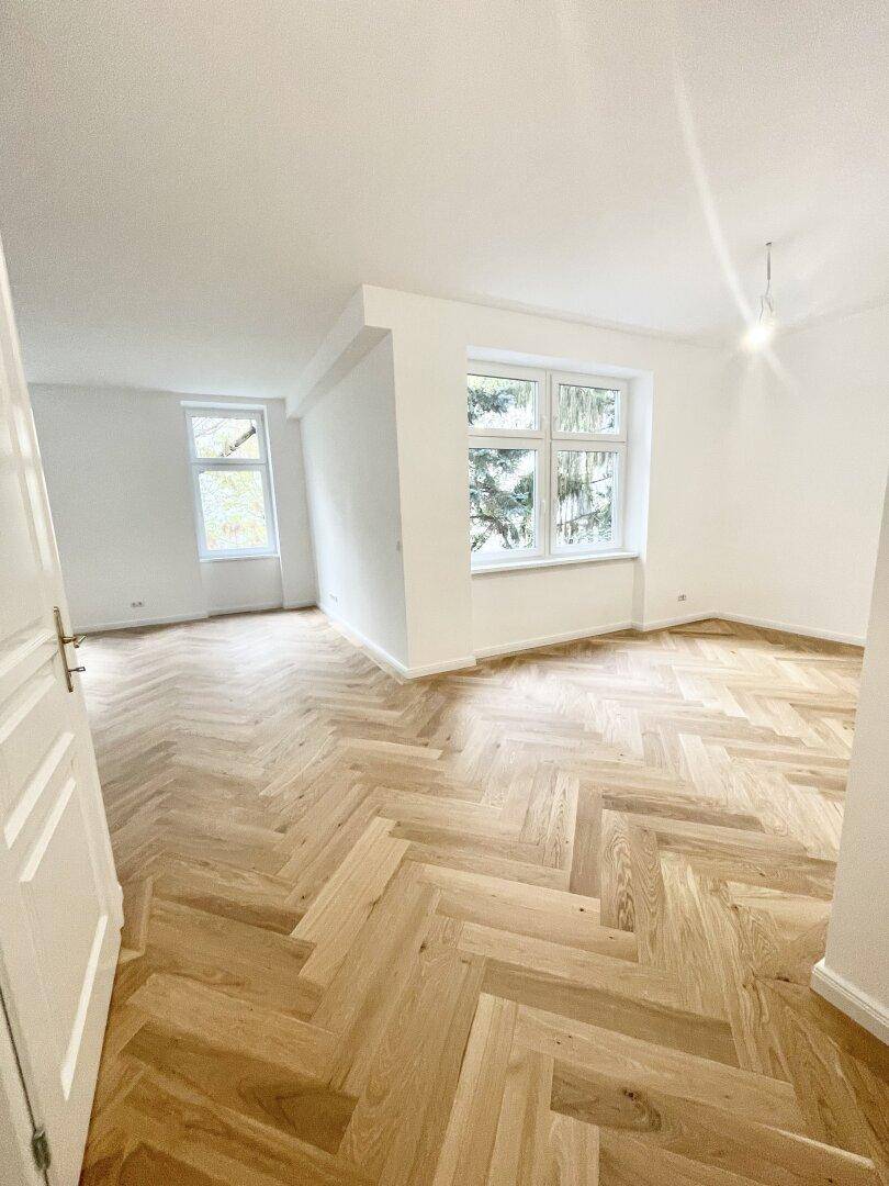 Heller, leerer Raum mit elegantem Fischgrätparkett, weißen Wänden und großen Fenstern.