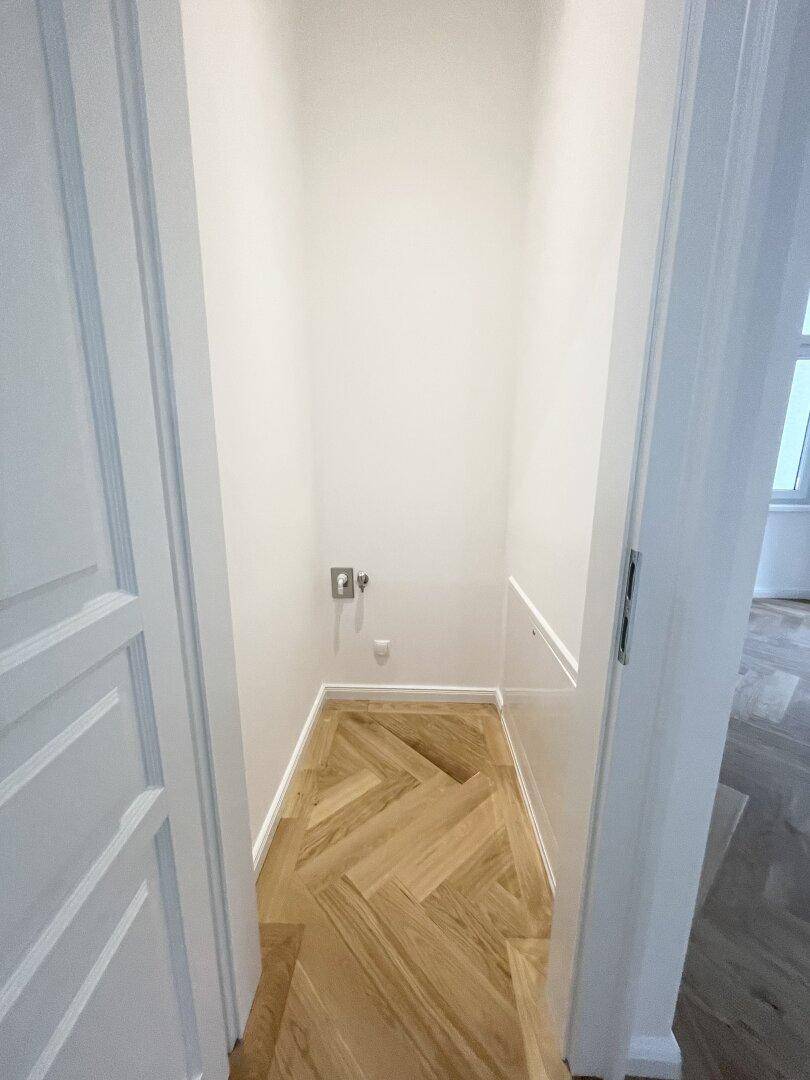 Kleiner Abstellraum mit Fischgrätparkett und Anschlüssen für eine Waschmaschine.