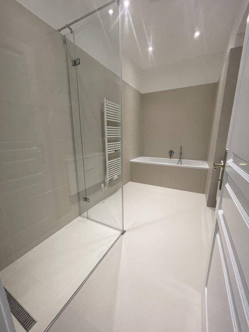 Modernes Badezimmer mit begehbarer Dusche, Badewanne, beheiztem Handtuchhalter und hellen Fliesen.