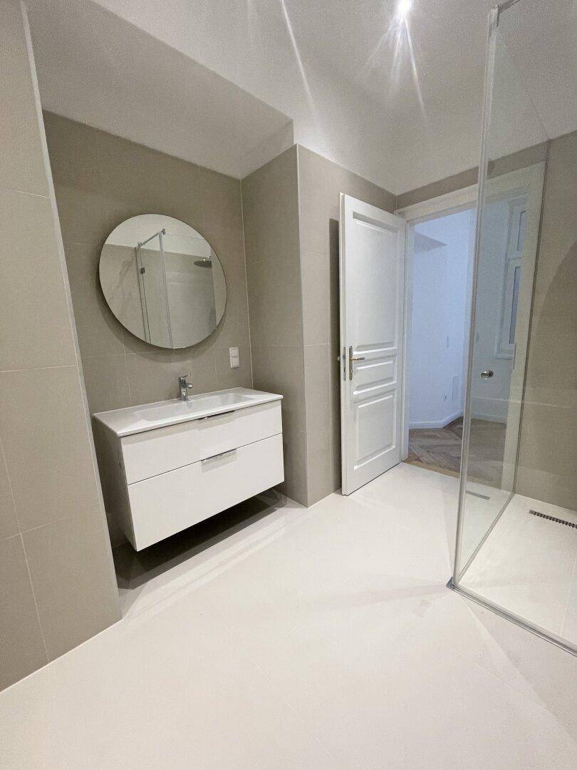 Modernes Badezimmer mit schwebendem Waschtisch, rundem Spiegel und begehbarer Dusche.