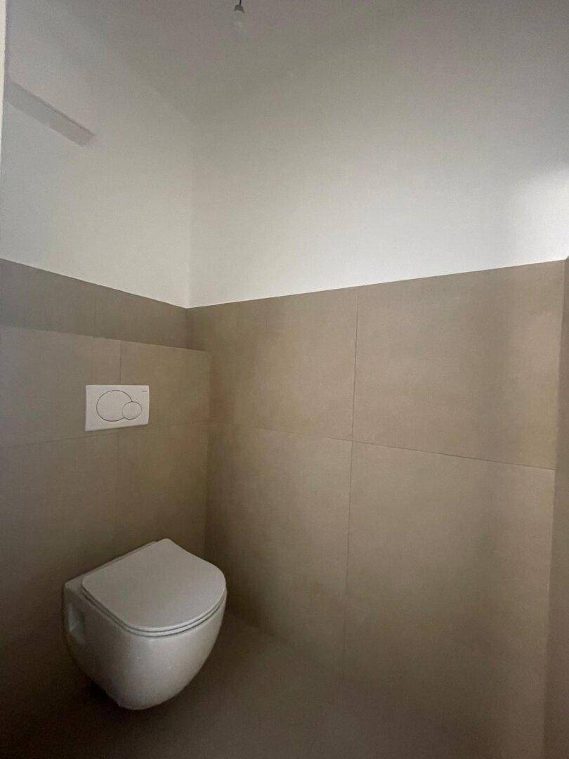 Separates WC mit wandhängender Toilette und modernen Fliesen an den Wänden.