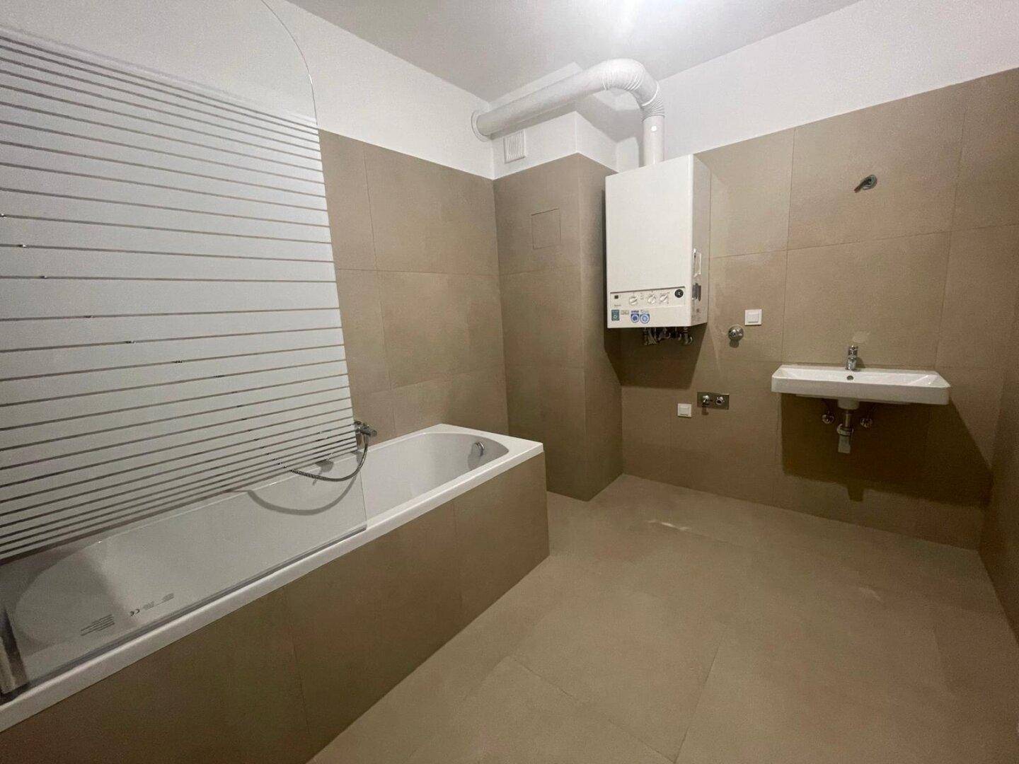 Funktionales Badezimmer mit beigefarbenen Fliesen, Badewanne und wandmontiertem Waschbecken.