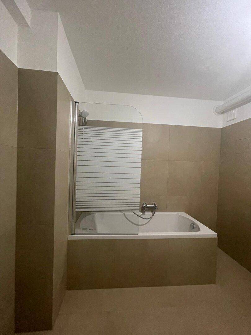 Badezimmer mit Badewanne und praktischer Duschabtrennung in neutralen Farbtönen.