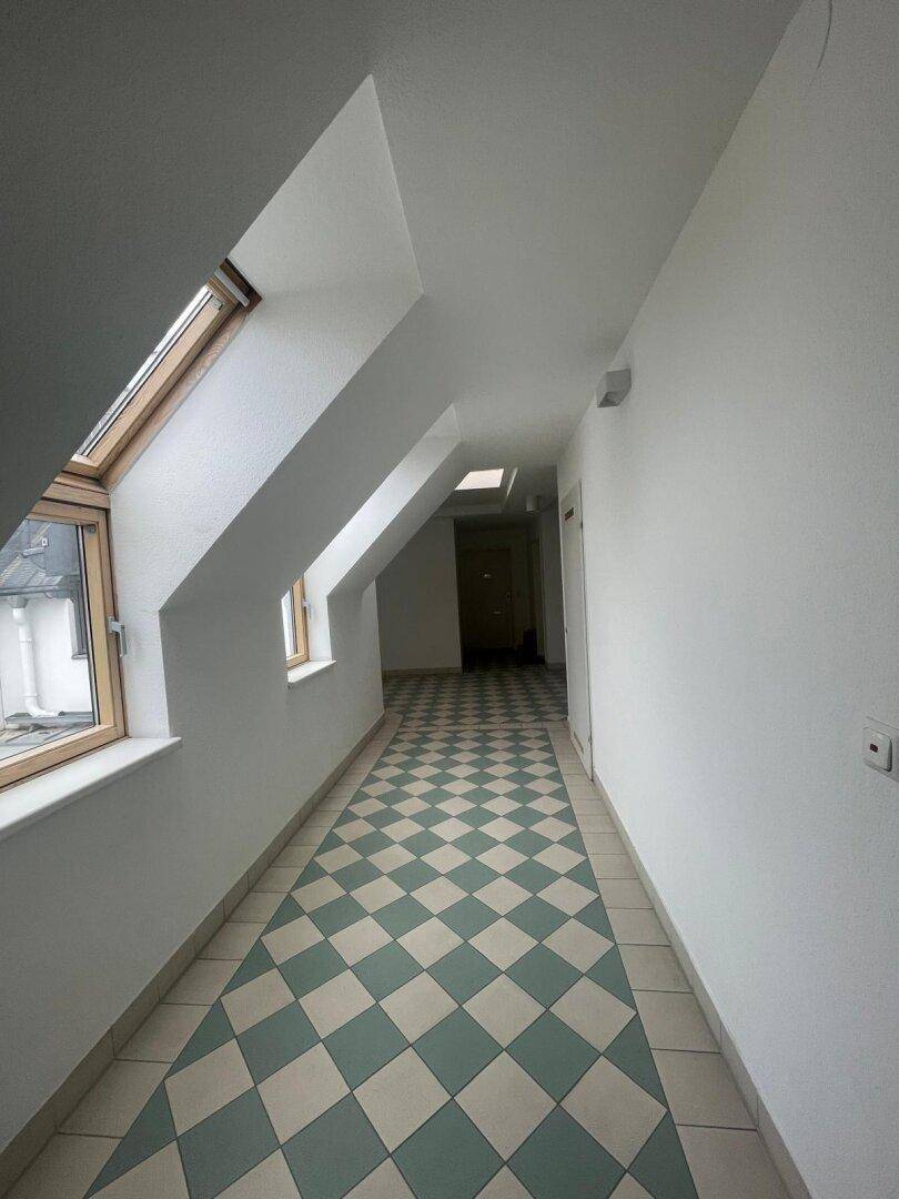 Heller Flur mit auffälligem Schachbrettmuster-Fliesenboden, Dachschrägen und Dachfenstern.