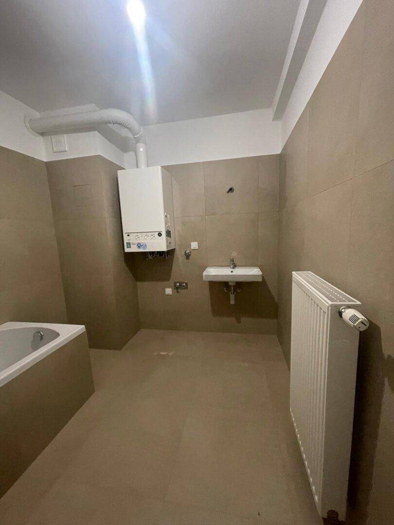 Badezimmer mit Heizkörper, Waschbecken und Badewanne, ausgestattet mit beigen Fliesen.