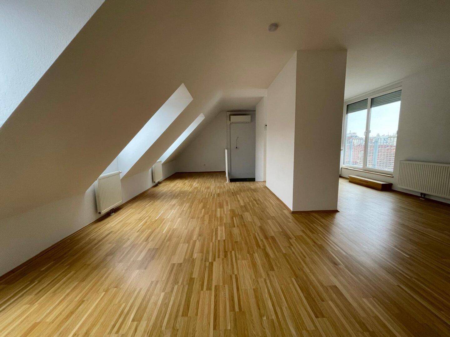 Geräumiger Wohnbereich mit Holzboden, Dachschrägen und großen Fenstern für viel Tageslicht.