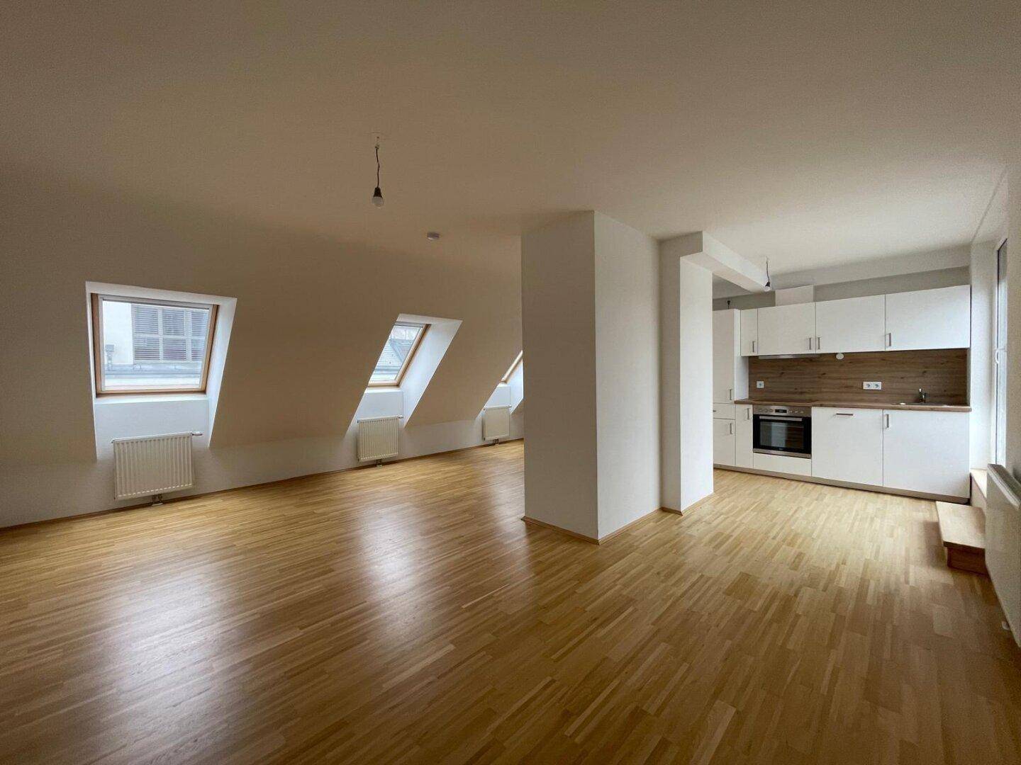 Heller offener Wohnbereich mit Holzboden, Dachschrägen und integrierter Küche.