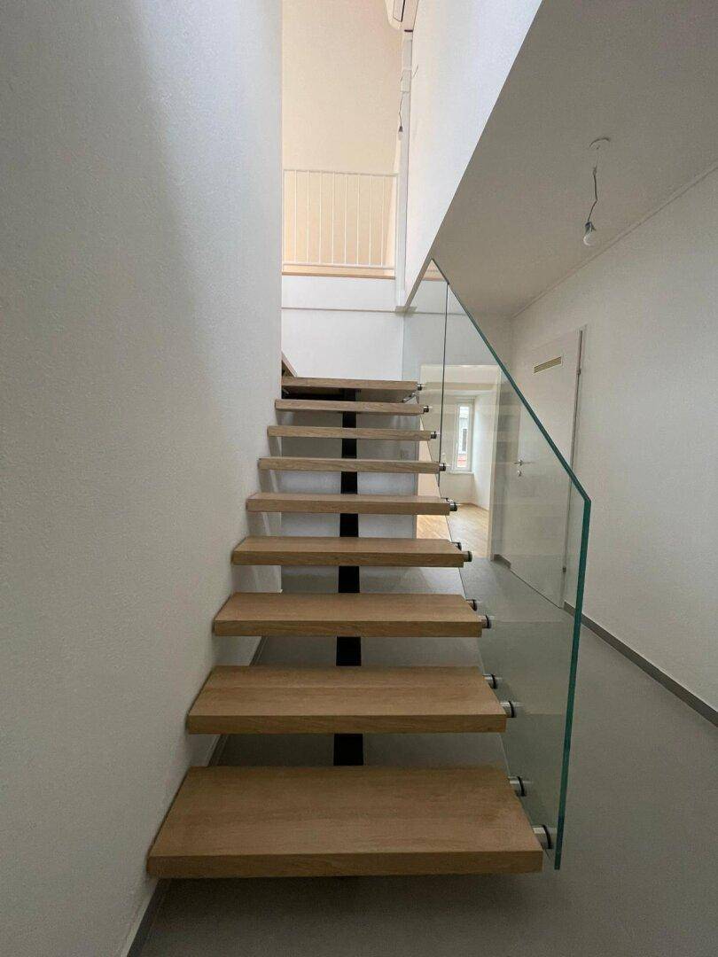 Moderne Holztreppe mit elegantem Glasgeländer, die zu den oberen Etagen führt.