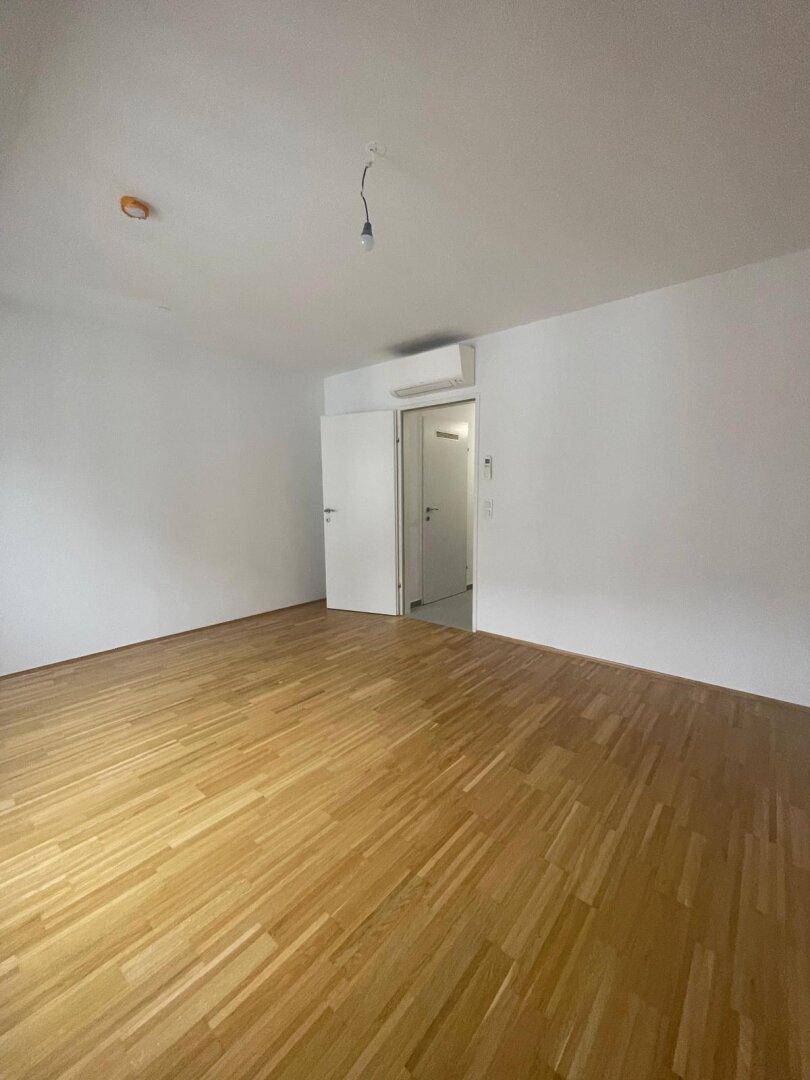 Helles Zimmer mit Holzboden und weißen Wänden, ausgestattet mit Klimaanlage.