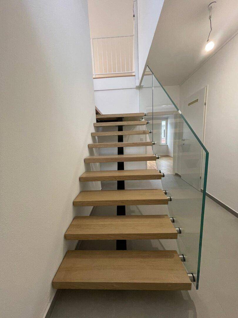 Moderne Holztreppe mit elegantem Glasgeländer, die zu den oberen Etagen führt.