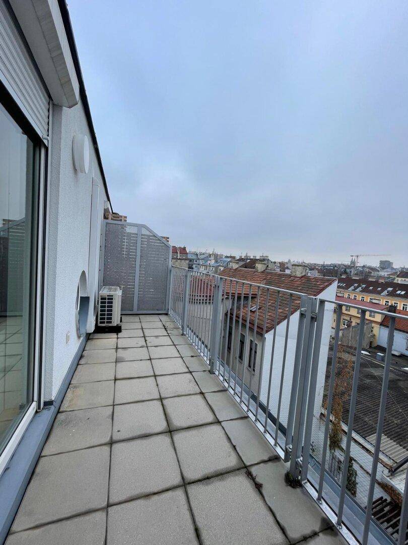 Langer Balkon mit Fliesenboden und Metallgeländer, bietet Blick über die Stadt.