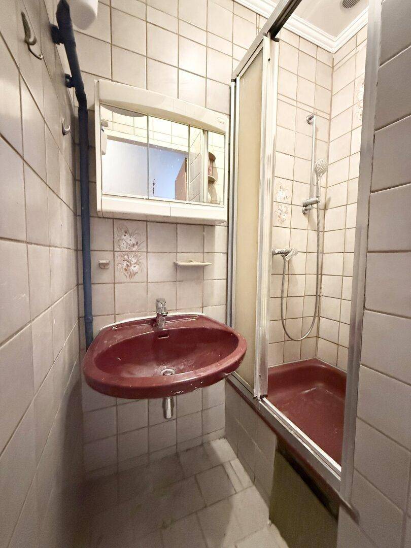 Kleines Badezimmer mit Fliesen, Waschbecken und einer Duschkabine.