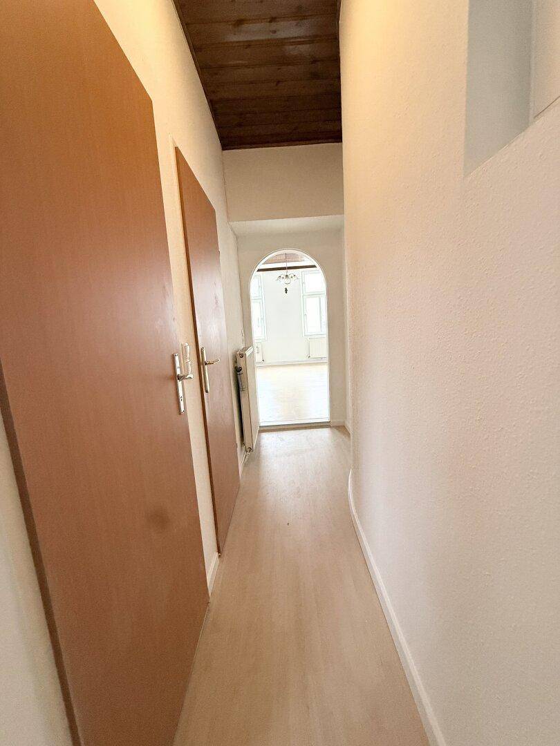 Schmaler Flur mit Holzbalkendecke, hellem Boden und braunen Türen.