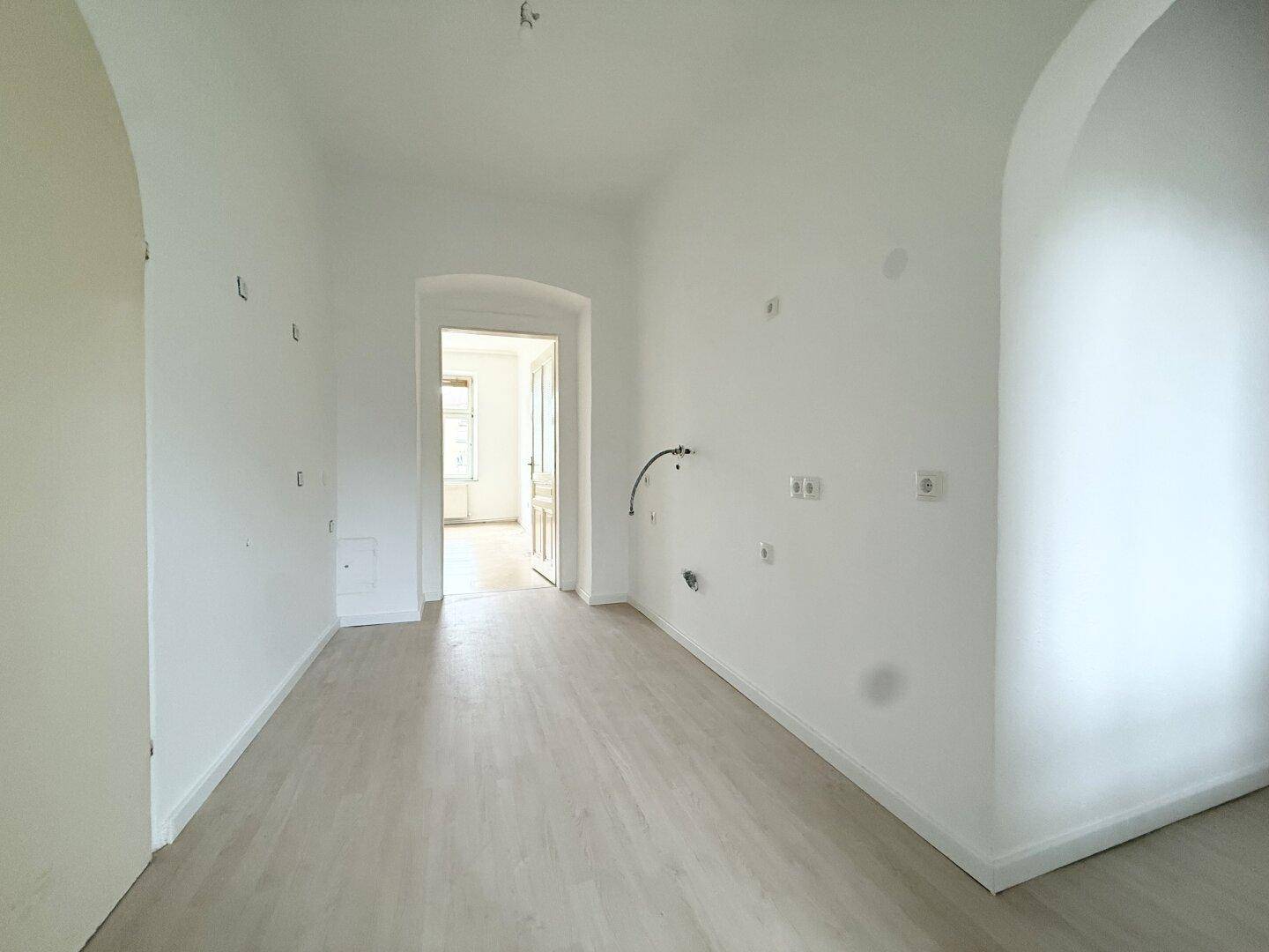 Heller Flur mit hellem Boden, weißen Wänden und einem eleganten Torbogen, der zu weiteren Räumen führt.