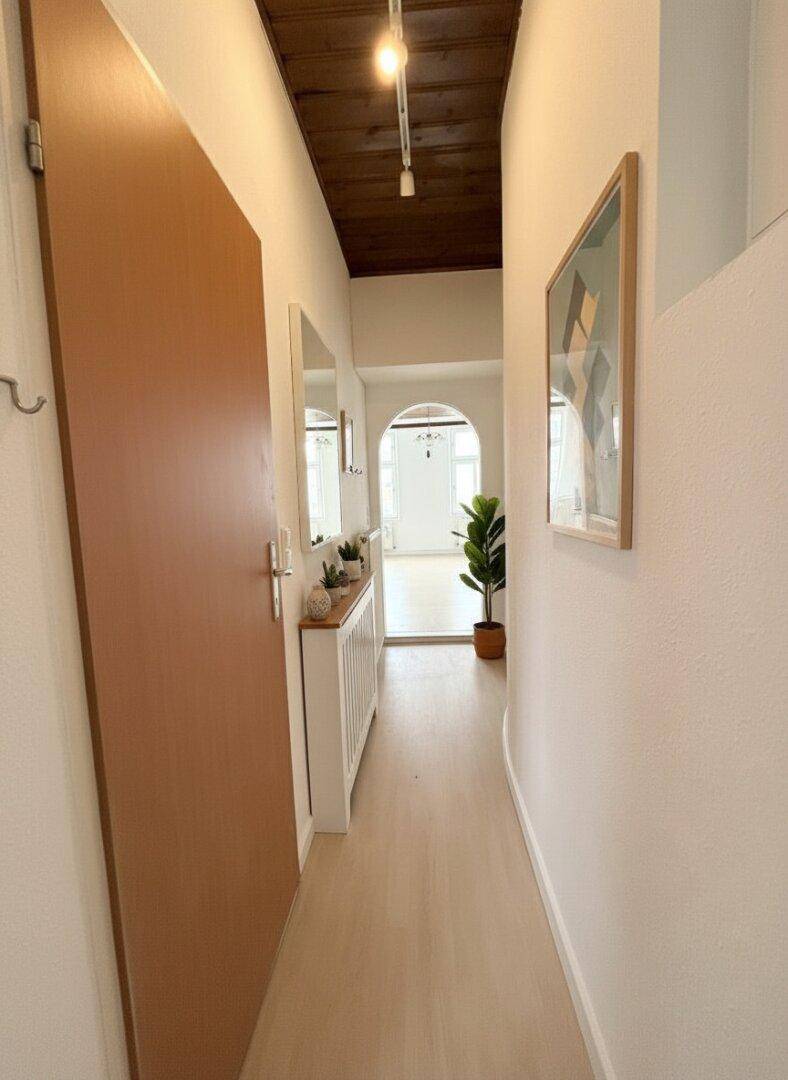 Freundlicher Flur mit Holzbalkendecke, hellem Boden und dekorativen Elementen.