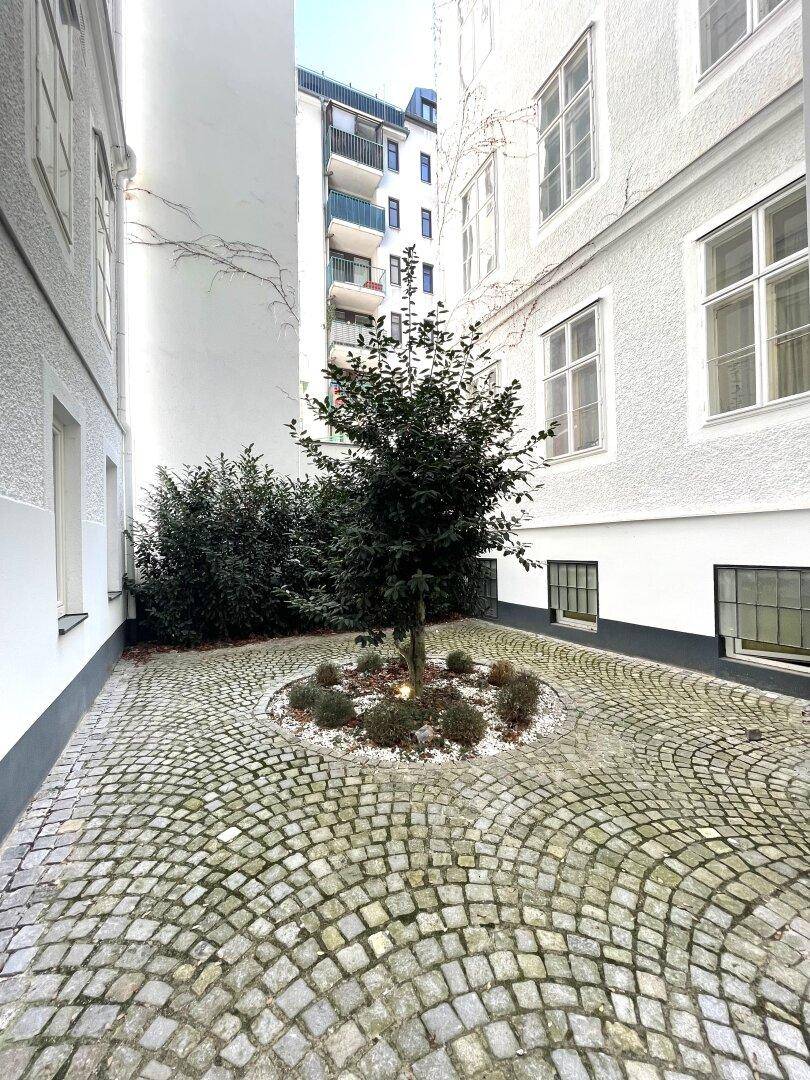 Ruhiger Innenhof mit Kopfsteinpflaster und einem zentralen Baum, umgeben von Gebäuden.