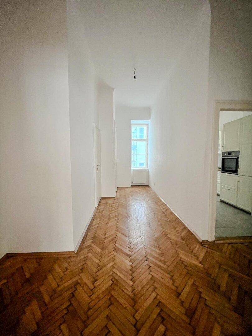 Heller Flur mit Fischgrätparkettboden, der den Blick in eine moderne Küche freigibt.
