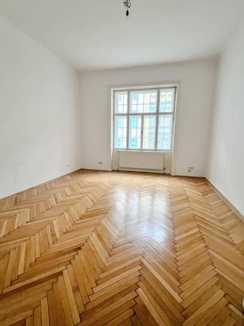 Geräumiges Schlafzimmer mit Fischgrätparkettboden und einem großen Fenster, das eine angenehme Atmosphäre schafft.