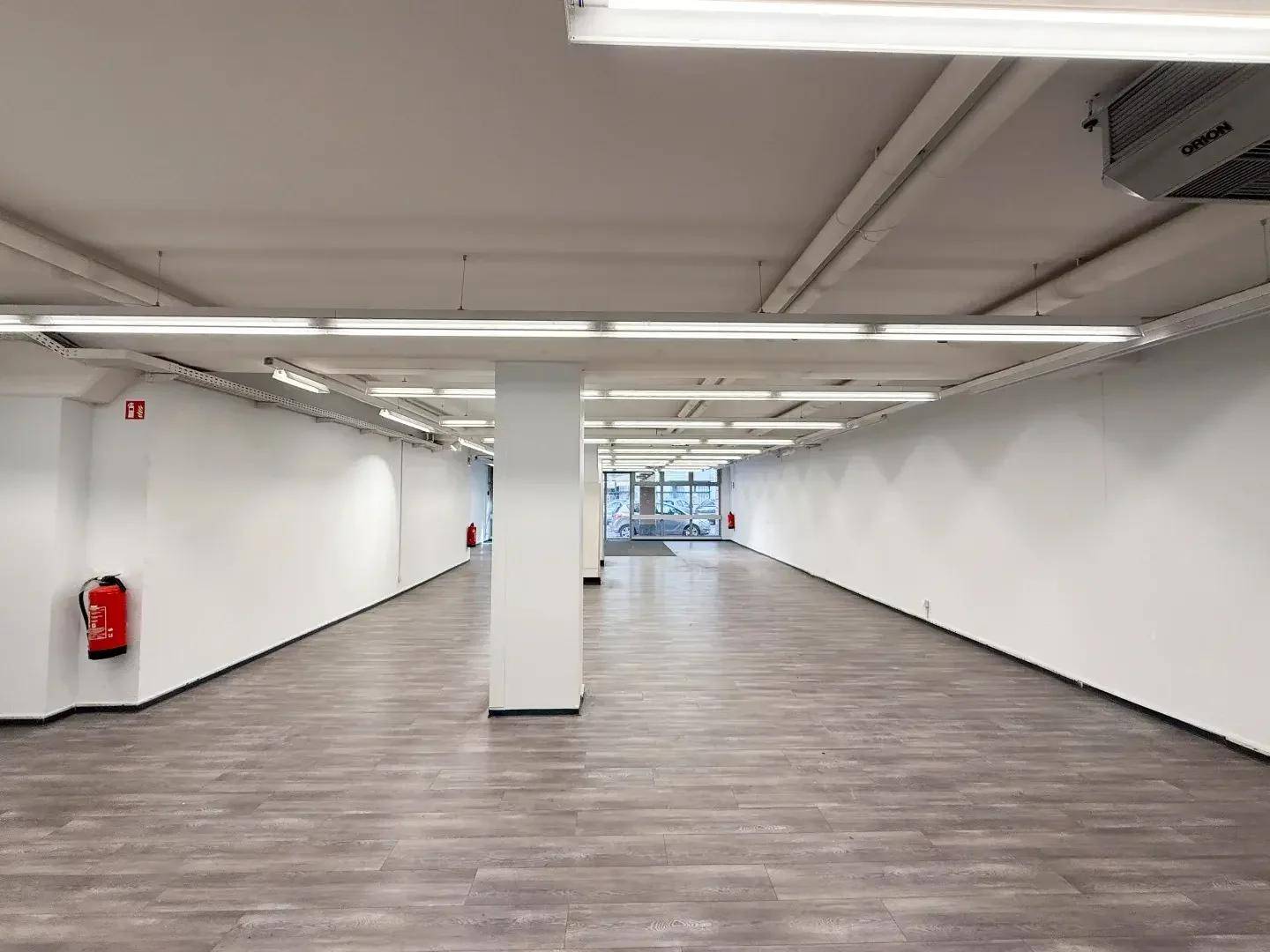 Geräumiger, leerer Ladenbereich mit modernem Bodenbelag, hohen Decken und viel Tageslicht durch die Schaufenster.