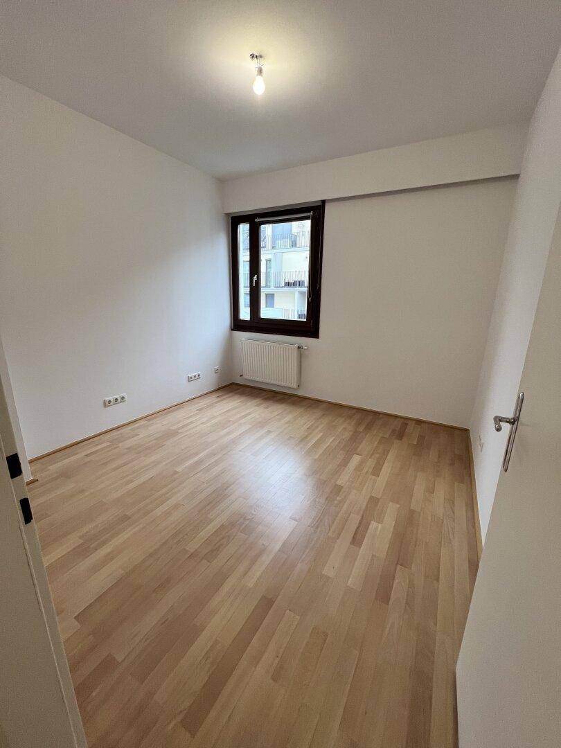 Helles Schlafzimmer mit Parkettboden und großem Fenster, bereit zur individuellen Gestaltung.