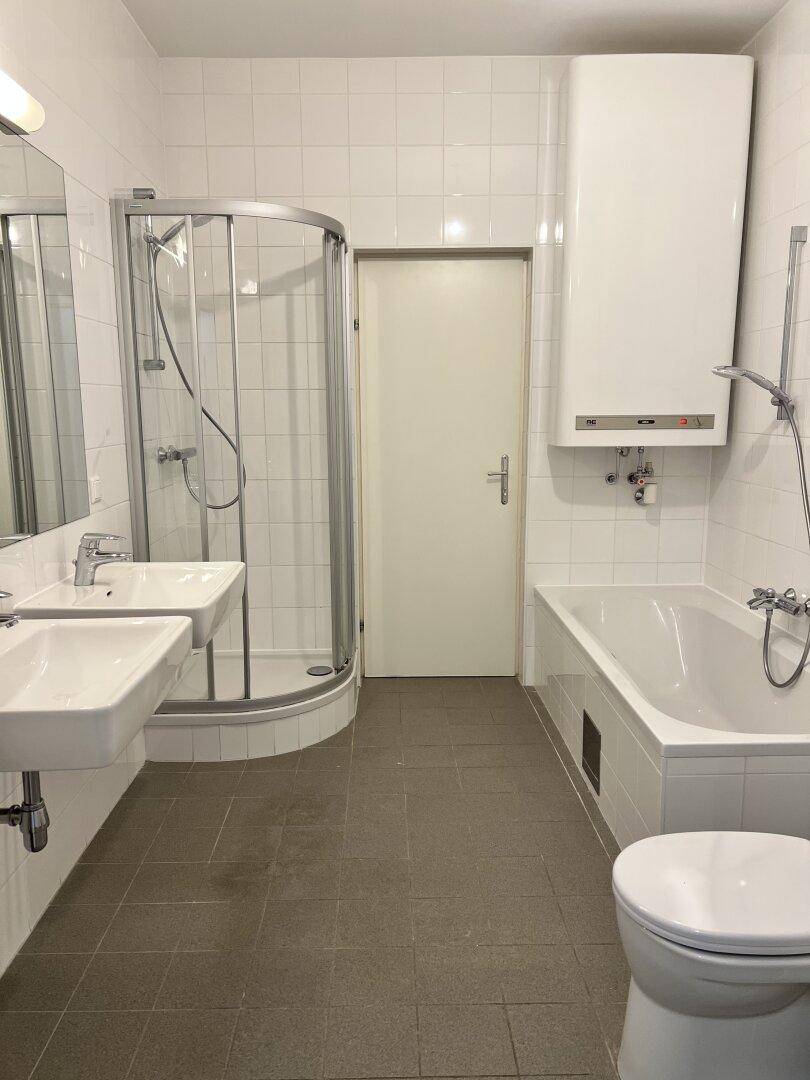 Modernes Badezimmer mit Badewanne, Dusche, Doppelwaschbecken und WC, hell gefliest.