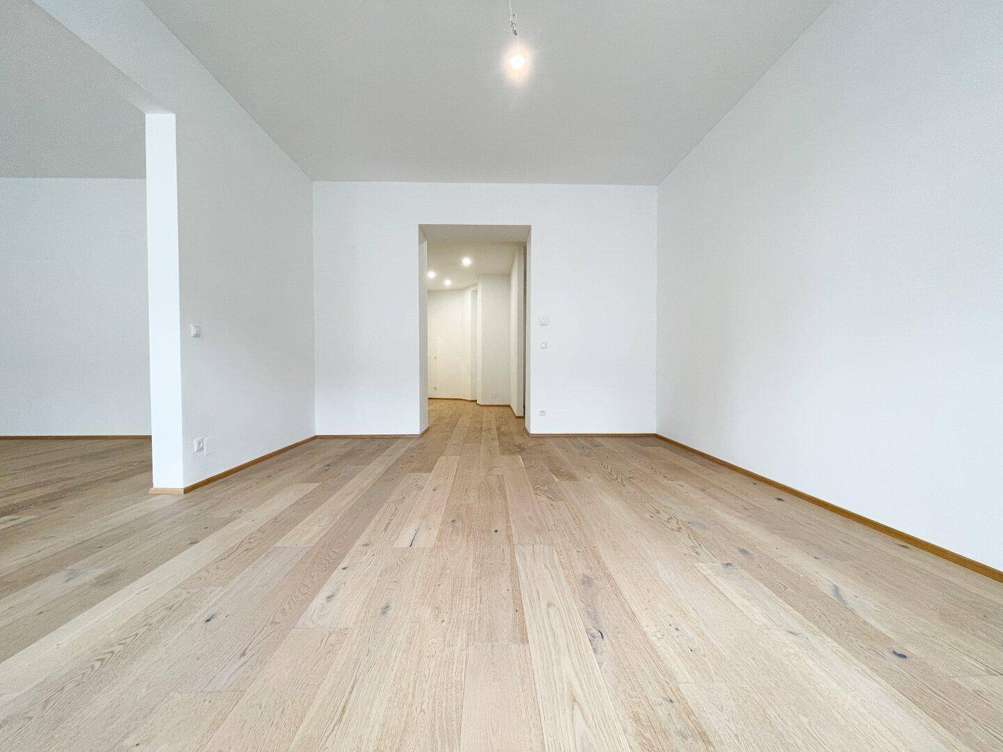 Geräumiger, heller Raum mit Parkettboden und einem offenen Zugang zu einem Flur.
