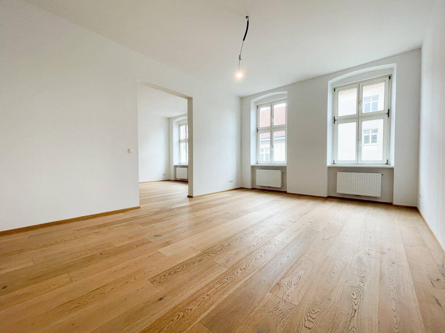 Lichtdurchfluteter Raum mit neuem Parkettboden und zwei Fenstern, ideal für Wohnzwecke.