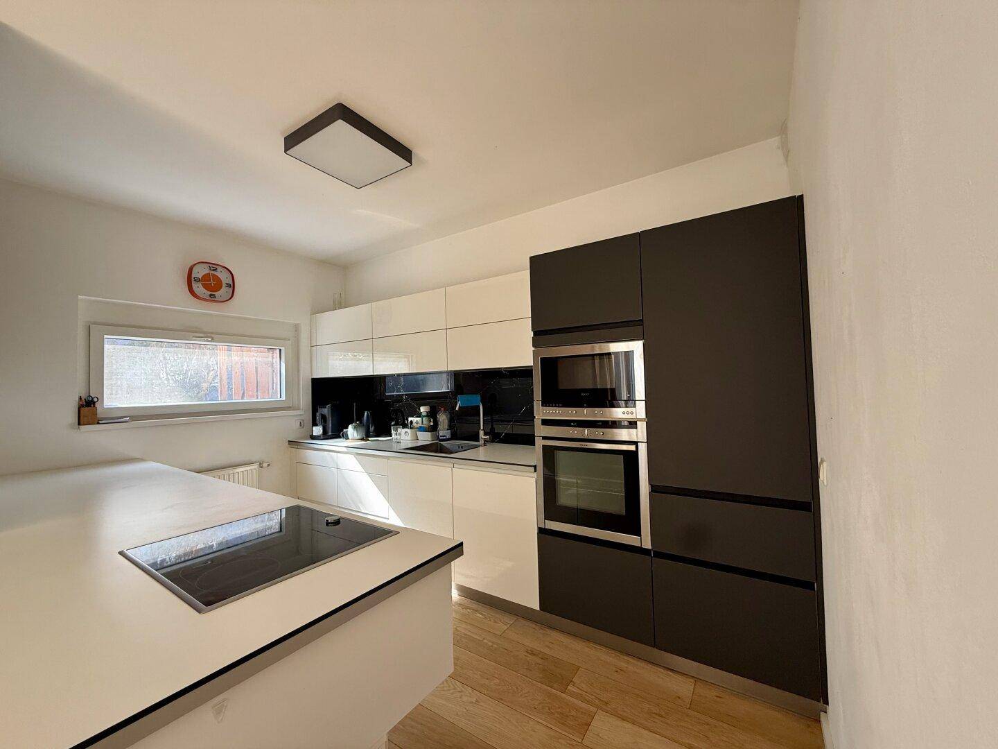 Moderne Einbauküche mit Kochinsel, Induktionskochfeld und integrierten Geräten in Schwarz-Weiß.