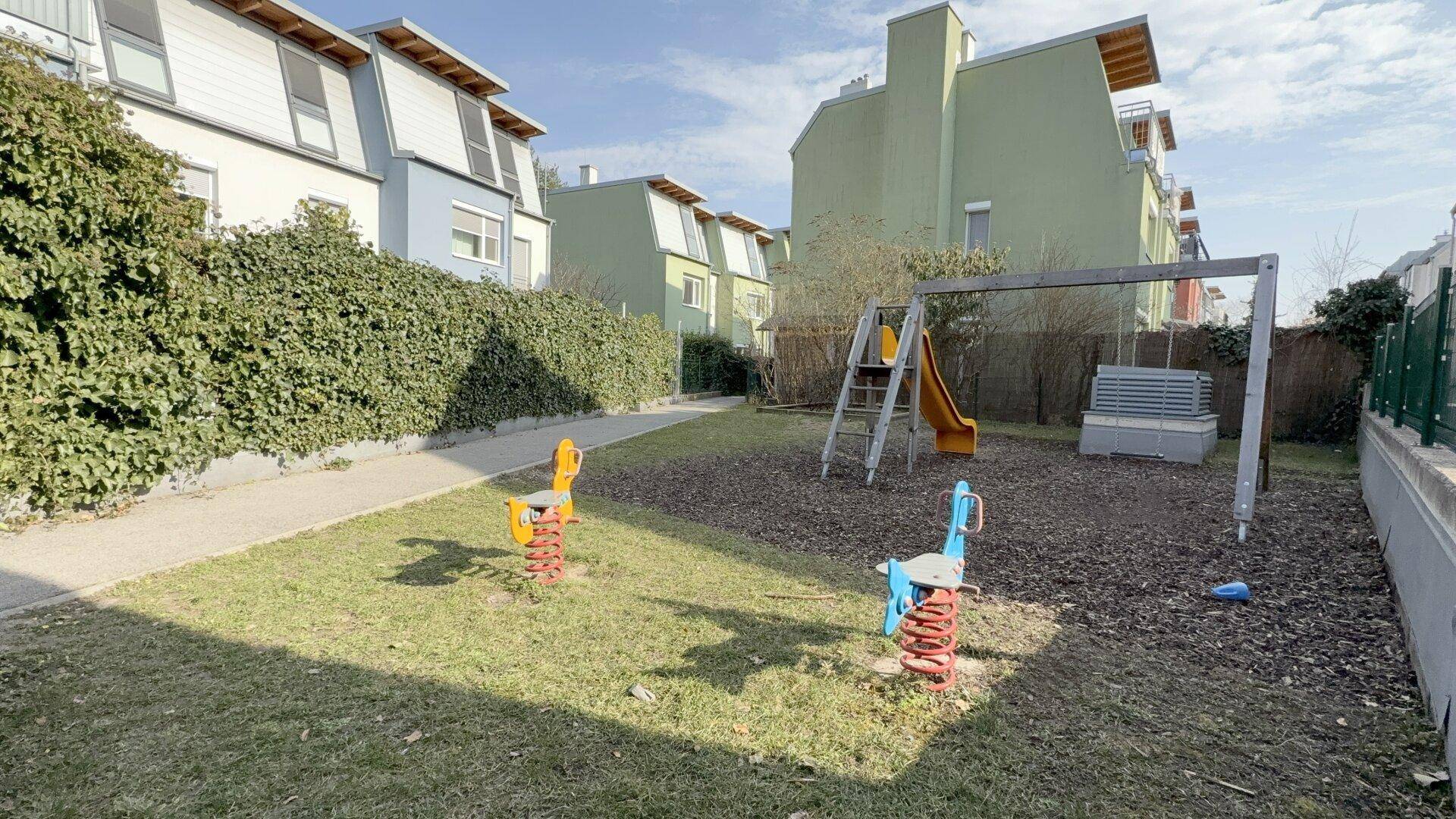 Gemeinschaftlicher Gartenbereich mit Spielplatz, Rutsche und Schaukeln für Kinder.