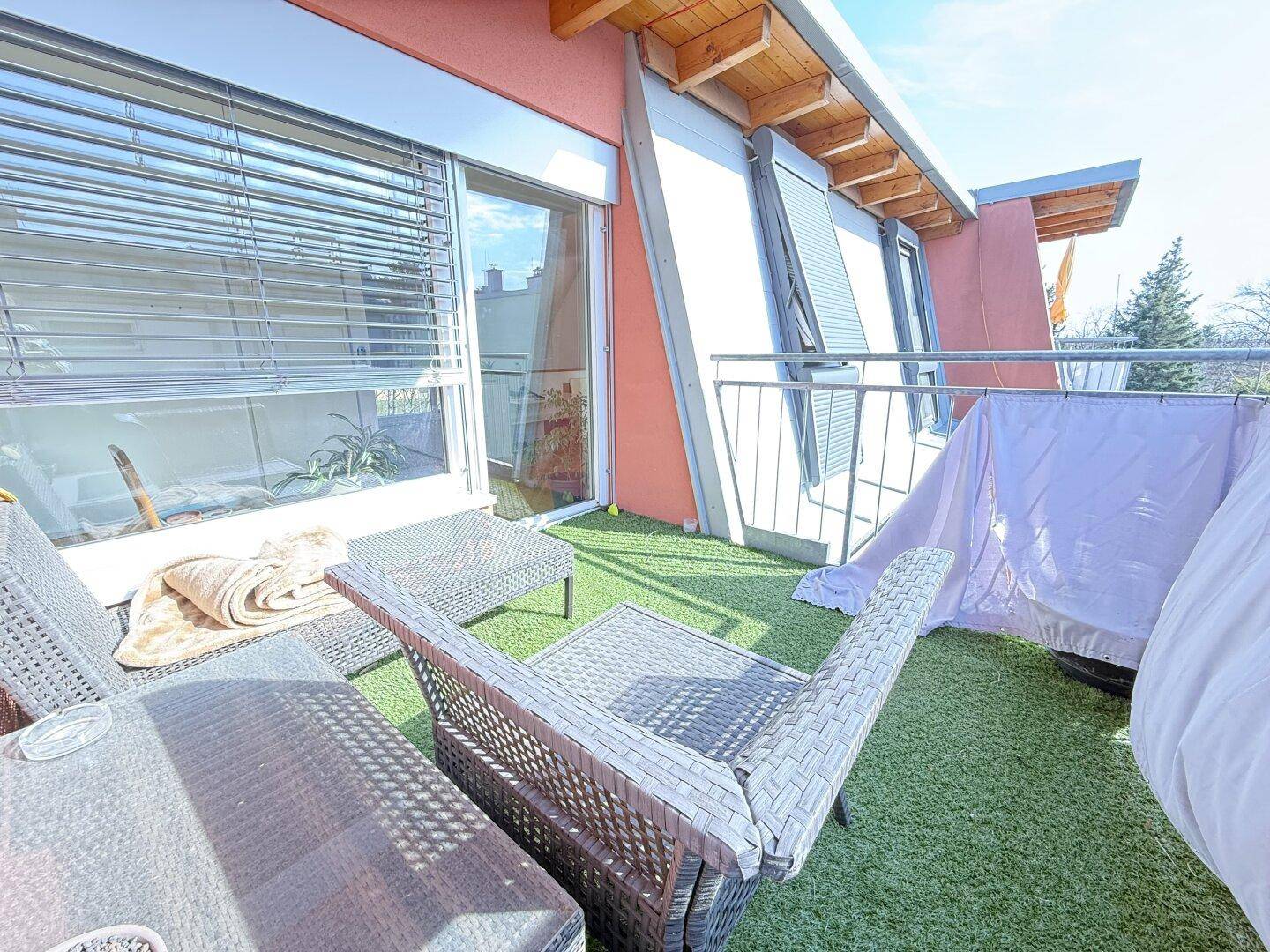 Sonniger Balkon mit Kunstrasen und Sitzgelegenheiten, ideal zum Entspannen im Freien.