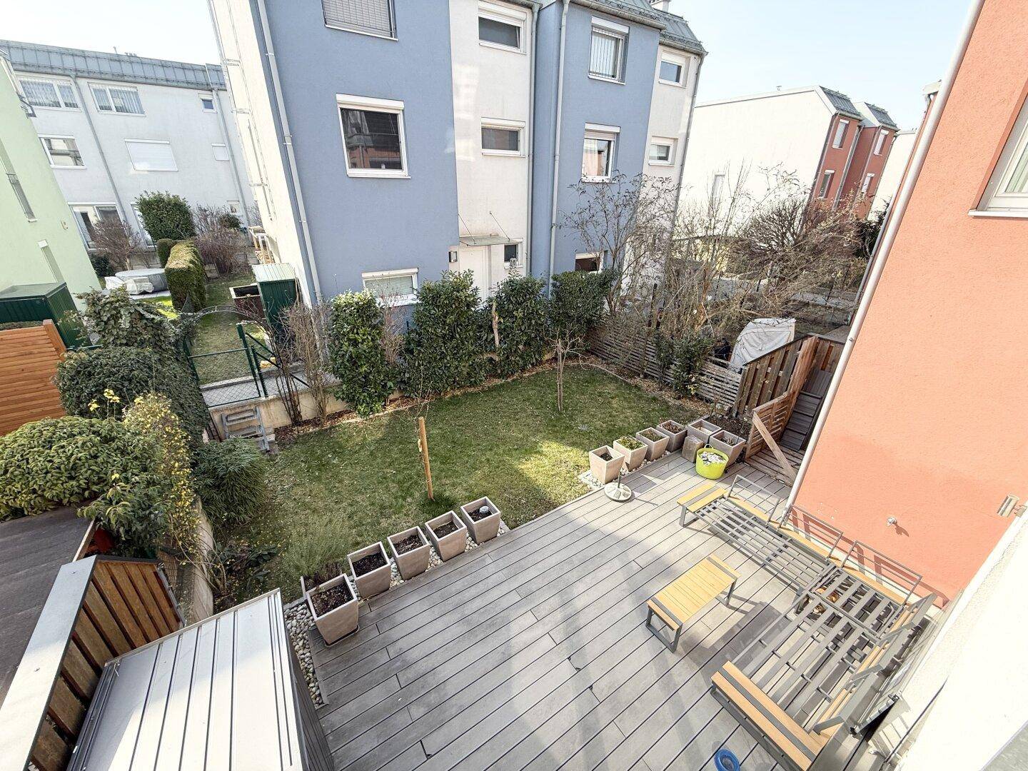 Vogelperspektive auf den gepflegten Garten mit Rasenfläche und großer Holzterrasse.