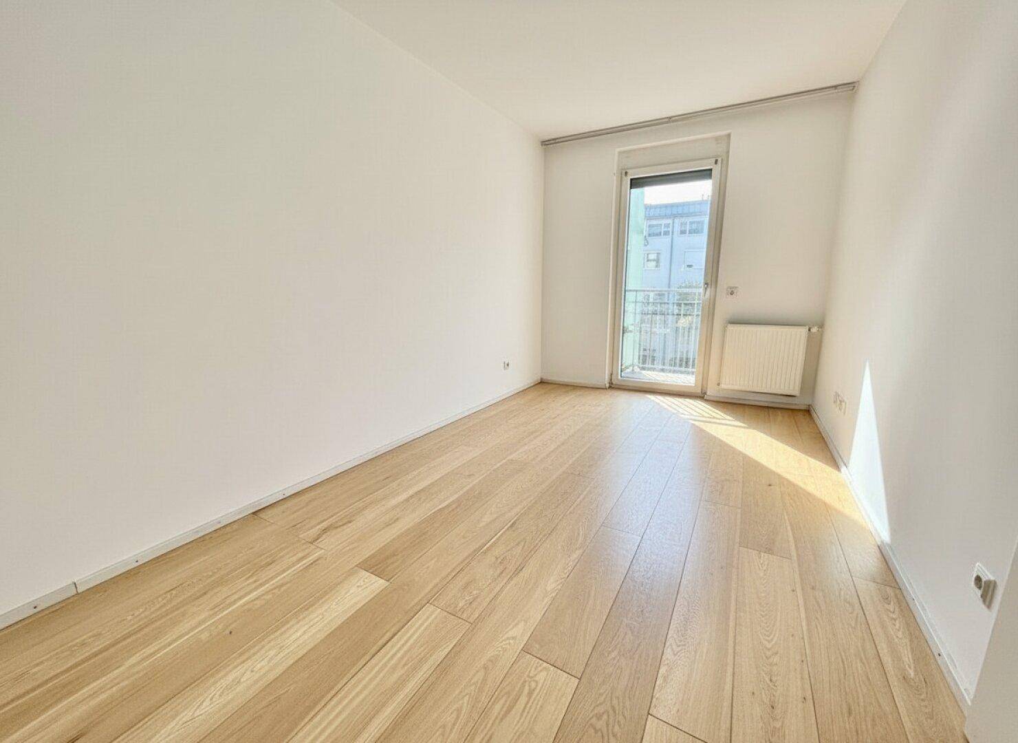 Freundliches Zimmer mit Holzboden und Zugang zu einem französischen Balkon, hell und einladend.