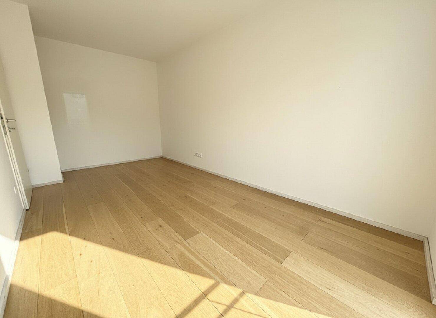 Leeres Zimmer mit Holzboden und viel Tageslicht, bereit zur individuellen Gestaltung.