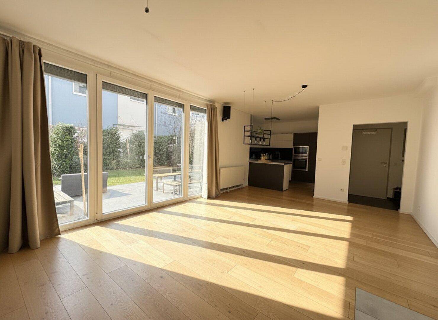 Lichtdurchfluteter Wohnbereich mit großen Fenstern, Holzboden und Zugang zur Terrasse.