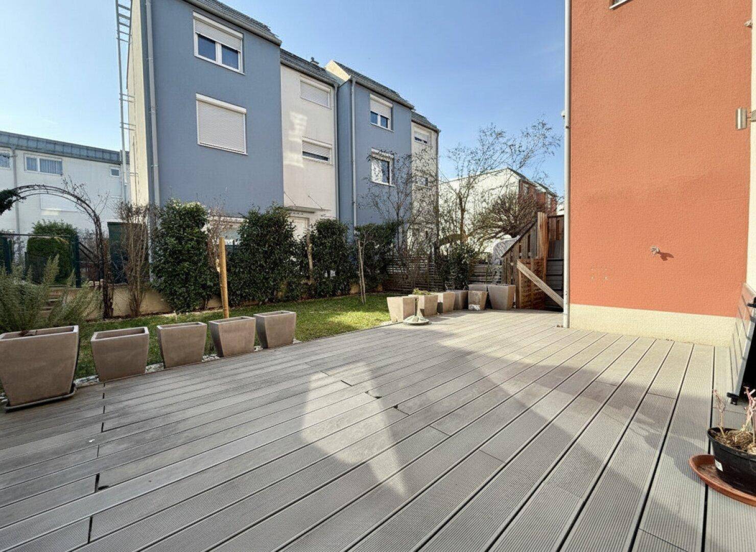Geräumige Holzterrasse mit Blick auf den Garten und die umliegenden Gebäude, ideal zum Entspannen.