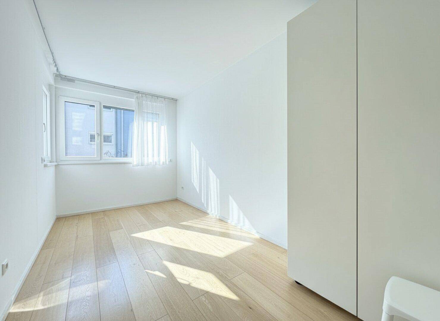 Helles Schlafzimmer mit Holzboden und großem Fenster, bietet viel Tageslicht und eine ruhige Atmosphäre.