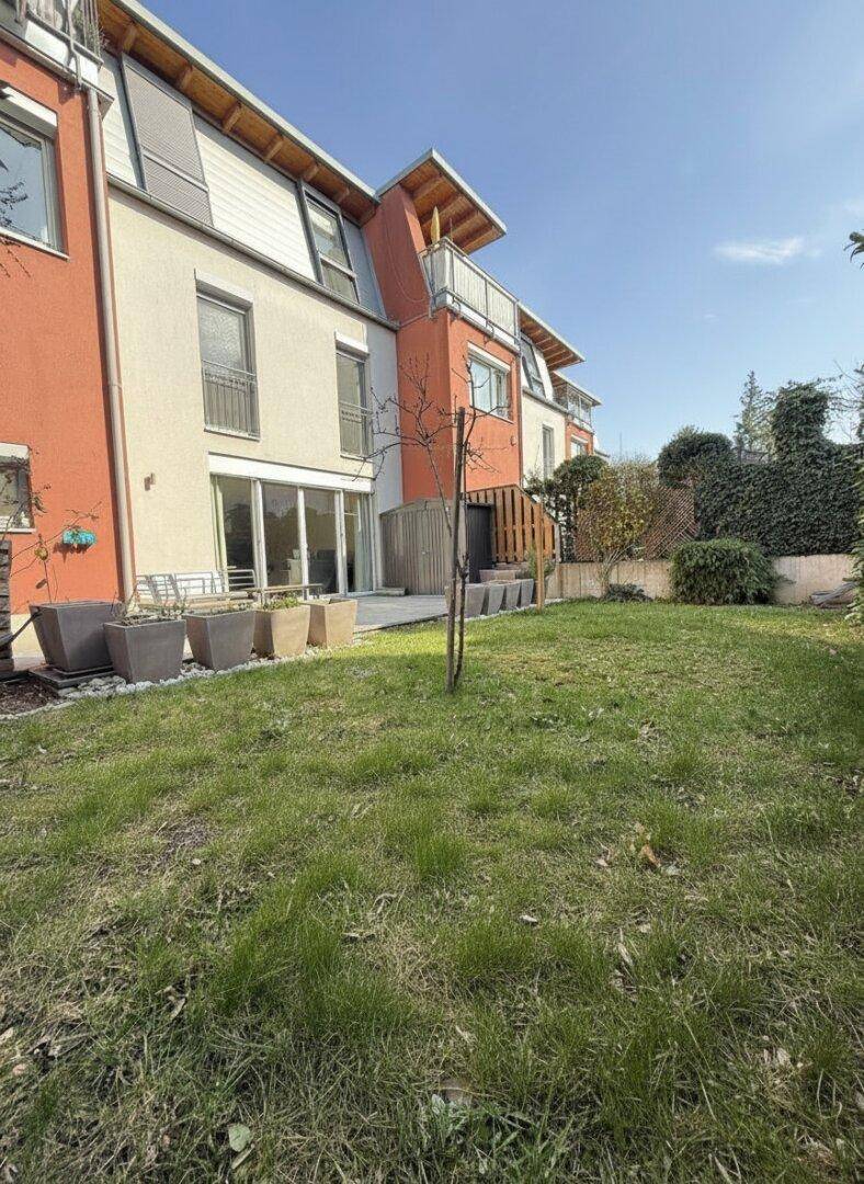 Gepflegter Gartenbereich mit Rasenfläche und angrenzender Terrasse hinter dem modernen Gebäude.