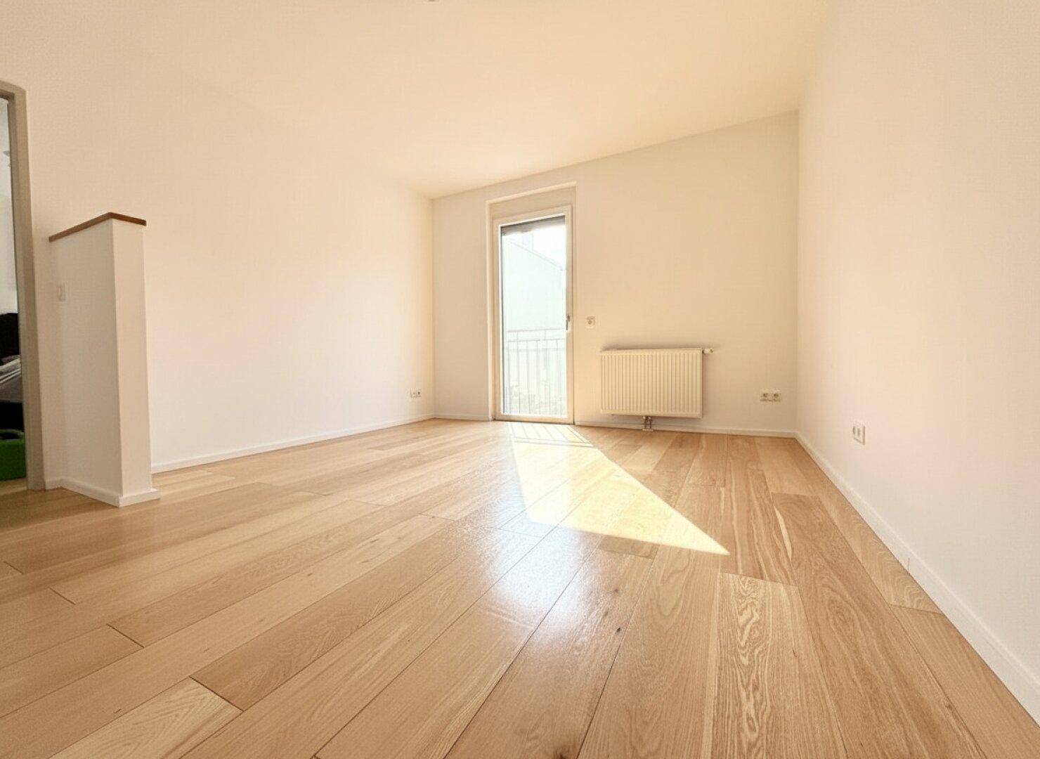 Helles Zimmer mit Holzboden und Zugang zu einem französischen Balkon, ideal als Schlaf- oder Arbeitszimmer.